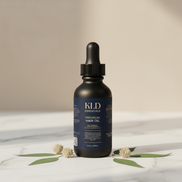 KLD Essentials premium hair oil bottle on a marble surface with leaves.